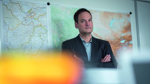 Jochen Bäcker vom LKA NRW steht mit verschränkten Händen in einem Büro. Im Hintergrund sind an einer Wand große Landkarten zu sehen.