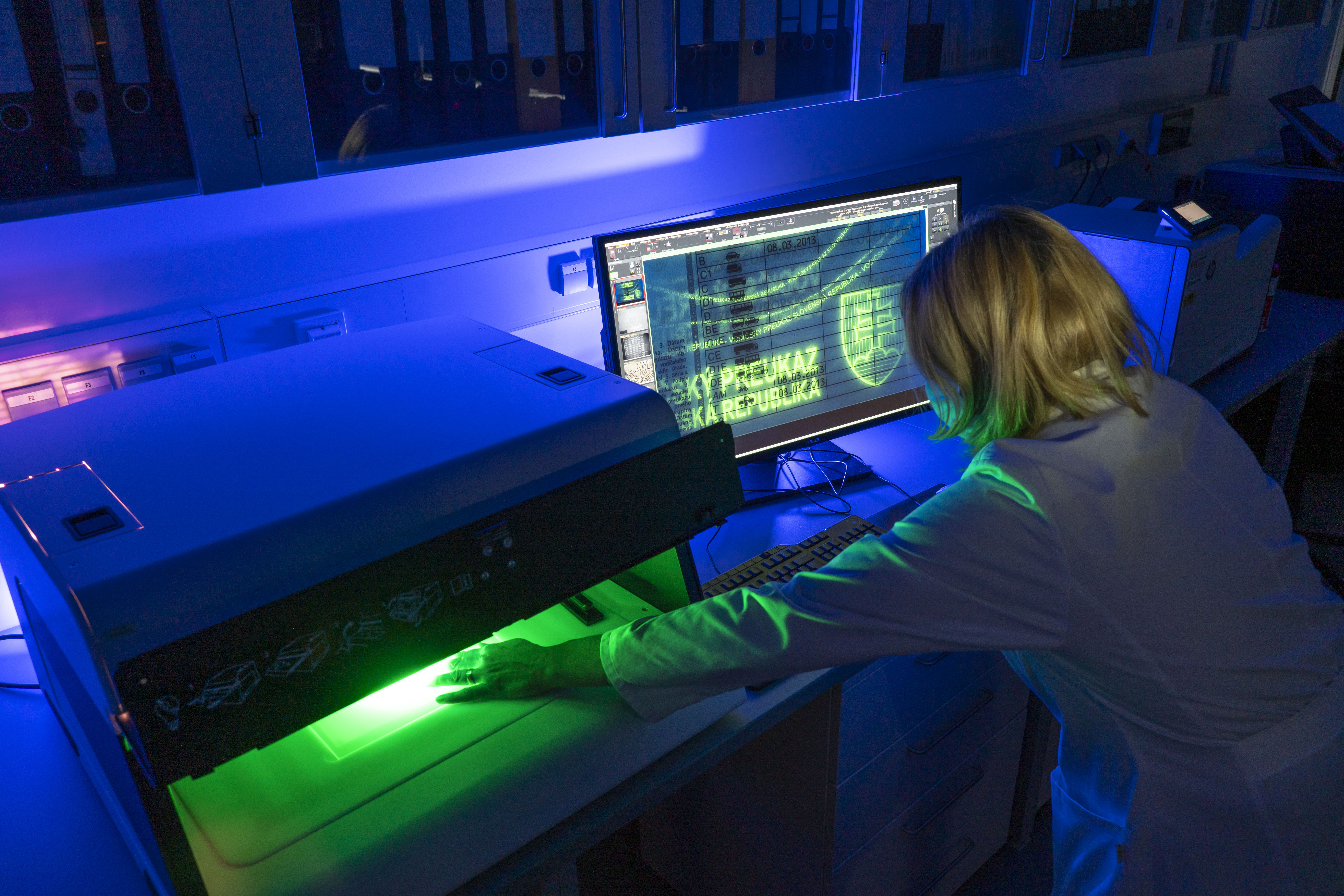 Mitarbeiterin am Computer, untersucht einen Pass unter speziellen Licht