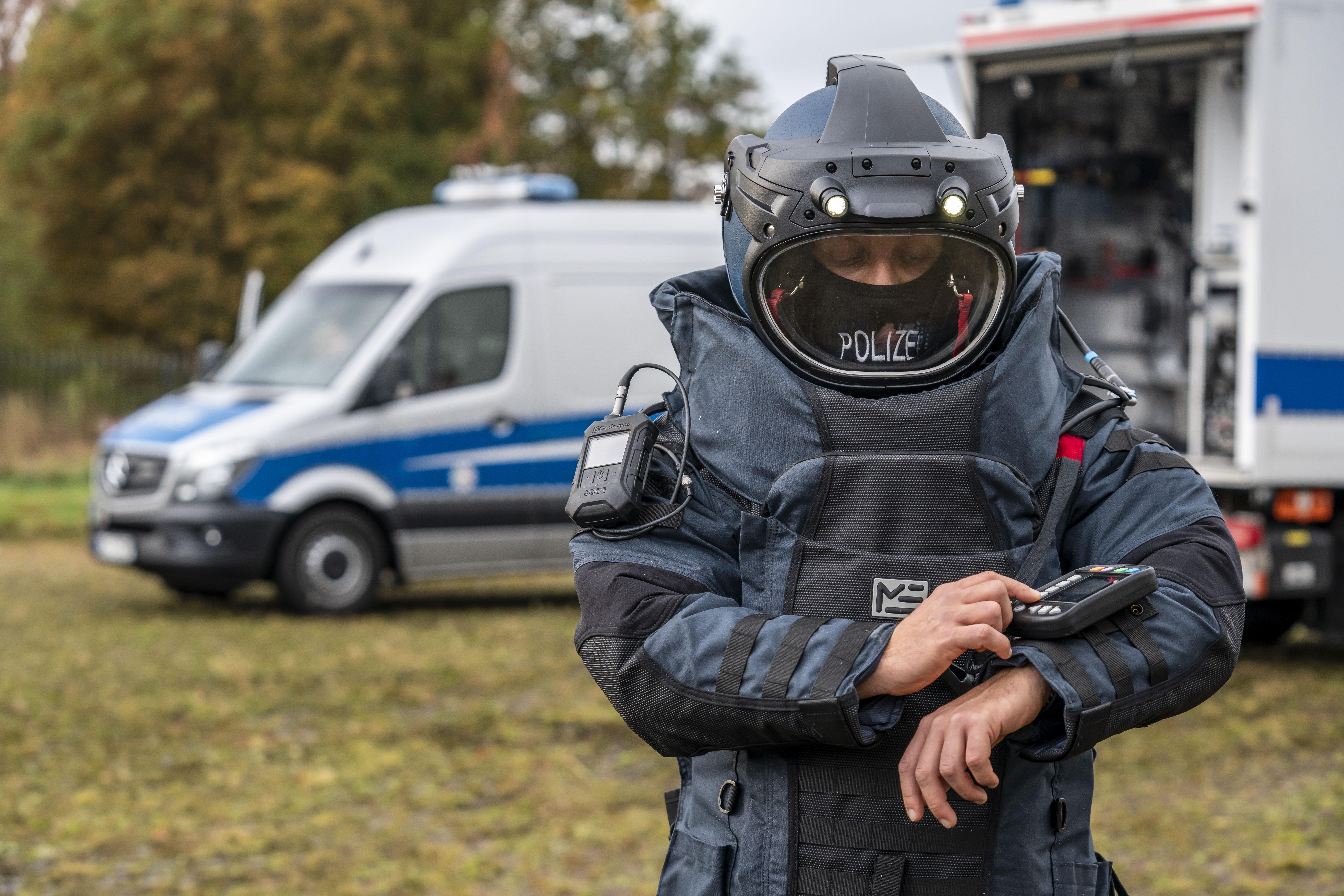 Entschärfer im Entschärferanzug vor Polizeifahrzeug