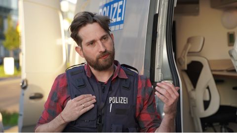 Ein Mitarbeiter des Cybercrime Kompetenzzentrums des LKA NRW steht im Vordergrund. Er spricht gerade über das MODAL-Fahrzeug, das im Hintergrund zu sehen ist.